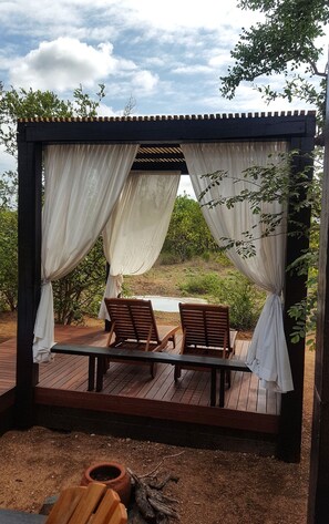 A wooden deck with two wooden chairs under a pergola with white curtains. - The Baobab Bush Lodge (Hoedspruit)
