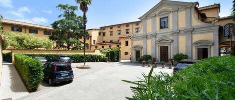A courtyard with parked cars, a building with classical architecture, and well-maintained greenery.