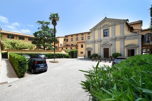 Un cortile con auto parcheggiate, un edificio dall'architettura classica e vegetazione curata.