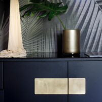 Un mobile blu scuro con due maniglie metalliche e un vaso dorato con una pianta verde.