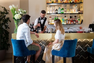 A bar area with a bartender preparing a drink, a woman seated, and a man seated across from her.