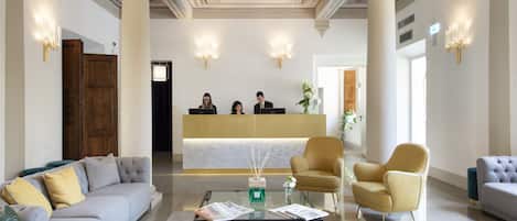 A lobby with a reception desk, sofas, a coffee table with magazines, and a chandelier.
