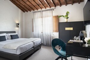 A bedroom with a bed, a desk with a computer, a chair, a plant, and a window with curtains.