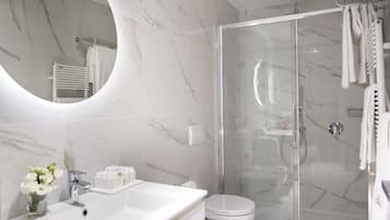 Un baño moderno con ducha de vidrio, un lavabo blanco con artículos de aseo y un espejo grande.