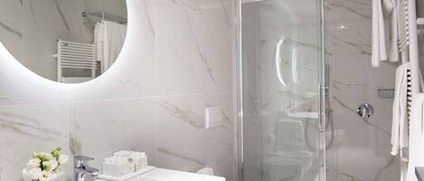 A modern bathroom with a glass-enclosed shower, a white sink with toiletries, and a large mirror.