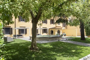 Un cortile con un albero, posti a sedere all'aperto e un edificio con diverse finestre e porte.
