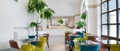 A modern restaurant with colorful chairs and tables, large windows, and potted plants.