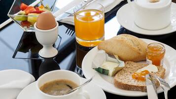 A breakfast setting with a variety of food items including toast, jam, butter, a cup of coffee, a glass of orange juice, a bowl of fruit, and a small egg.
