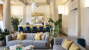 Una sala de estar moderna con un sofá gris, una zona de bar con un espejo para licores y plantas grandes en macetas.