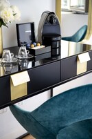 A modern hotel room with a sleek black and gold minibar, a coffee machine, and a teal chair.