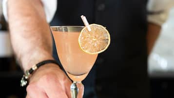 A person in a black vest and white shirt holding a cocktail with a lemon garnish.