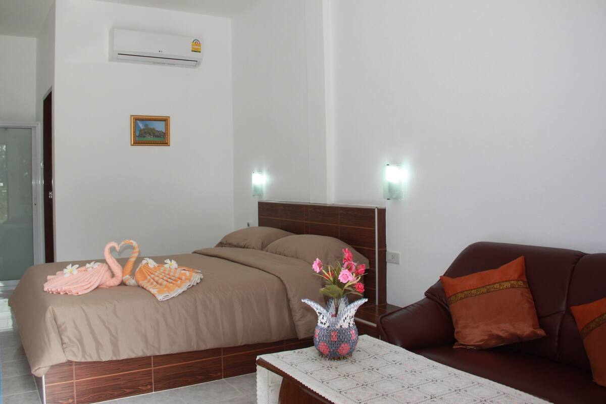 A hotel room with a bed, a sofa, a table with a vase of flowers, and wall-mounted lights.