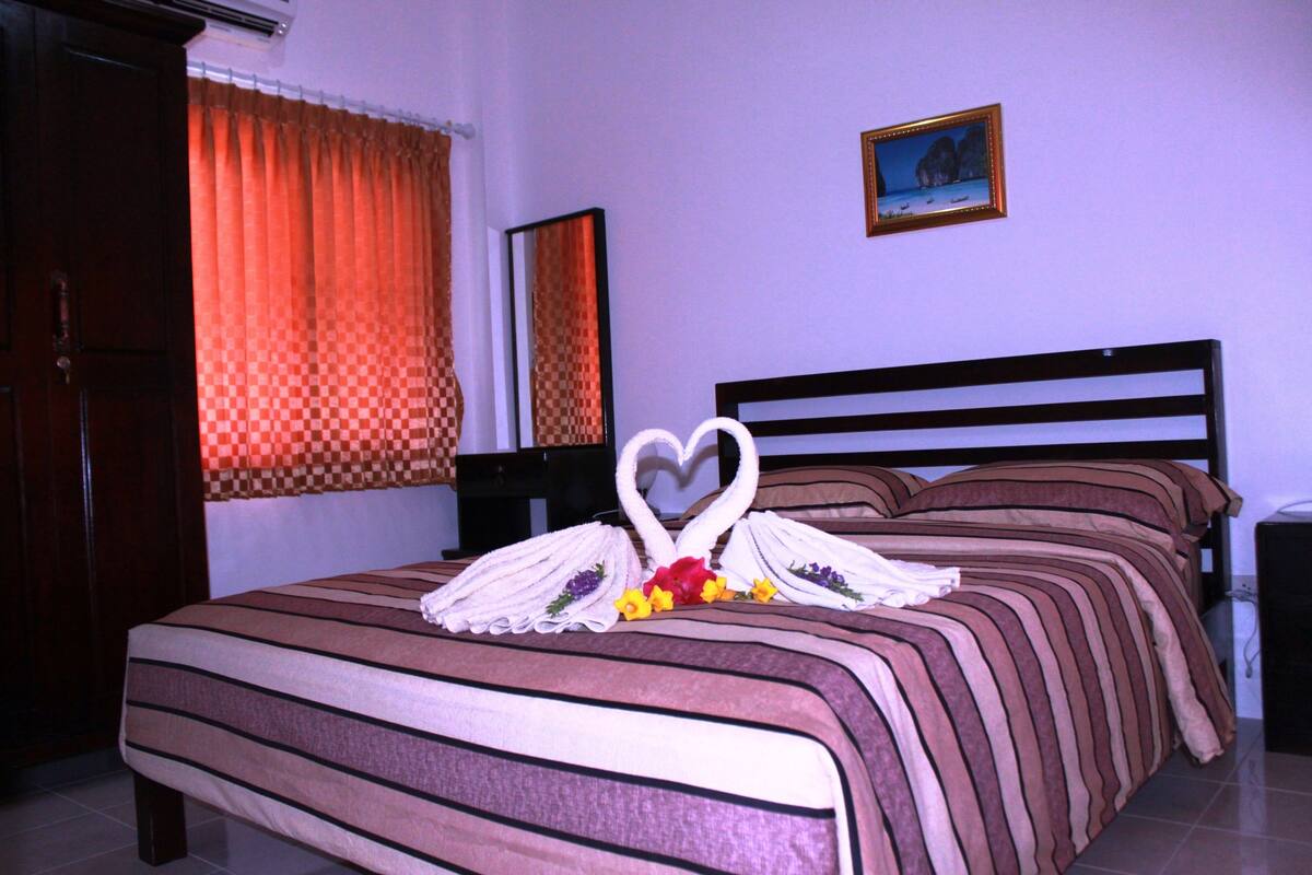 A neatly made bed with striped bedding, a heart-shaped towel arrangement, and a framed picture on the wall.