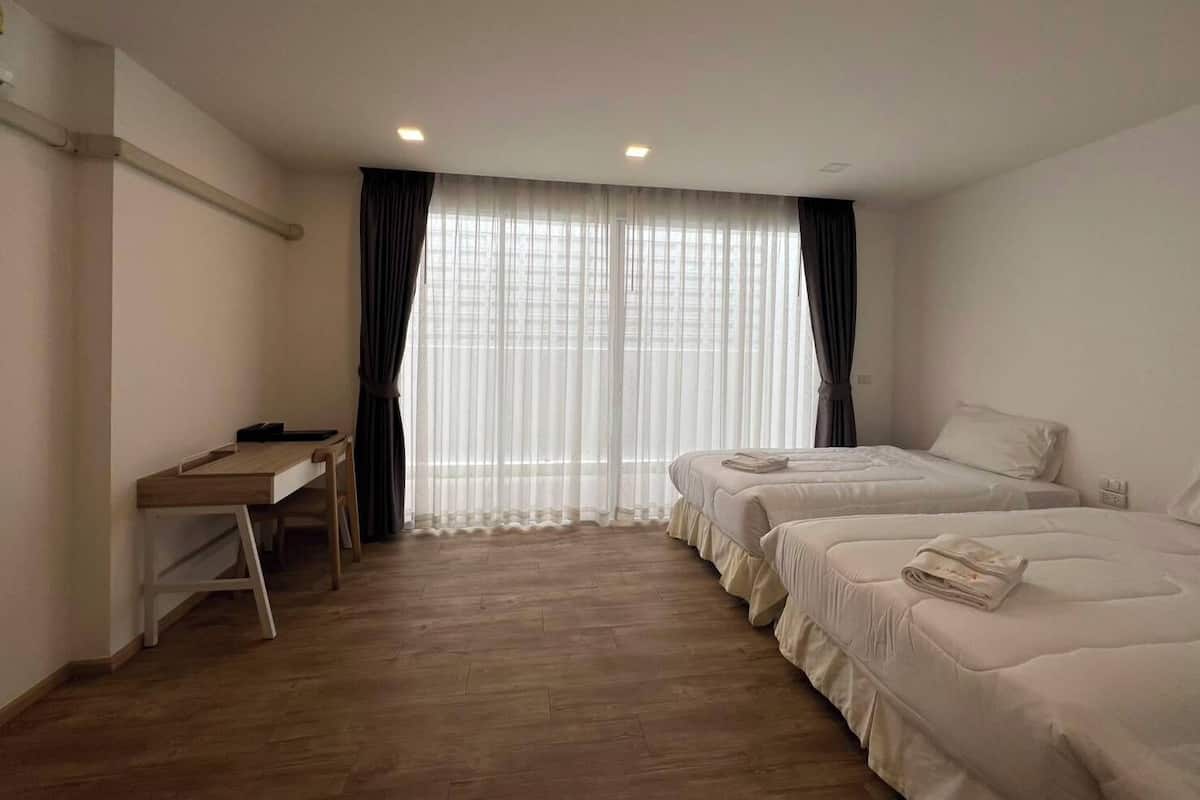 Een hotelkamer met twee bedden, een bureau en een raam met dunne gordijnen.
