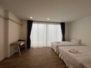Habitación de hotel con dos camas, un escritorio y una ventana con cortinas translúcidas.