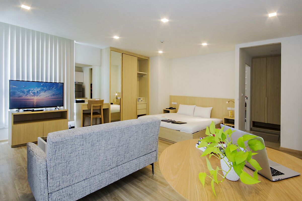 Una habitación de hotel moderna con una cama, un sofá, un escritorio con una computadora portátil, un televisor y una planta.