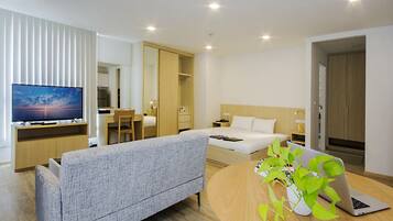 Una habitación de hotel moderna con una cama, un sofá, un escritorio con una computadora portátil, un televisor y una planta.