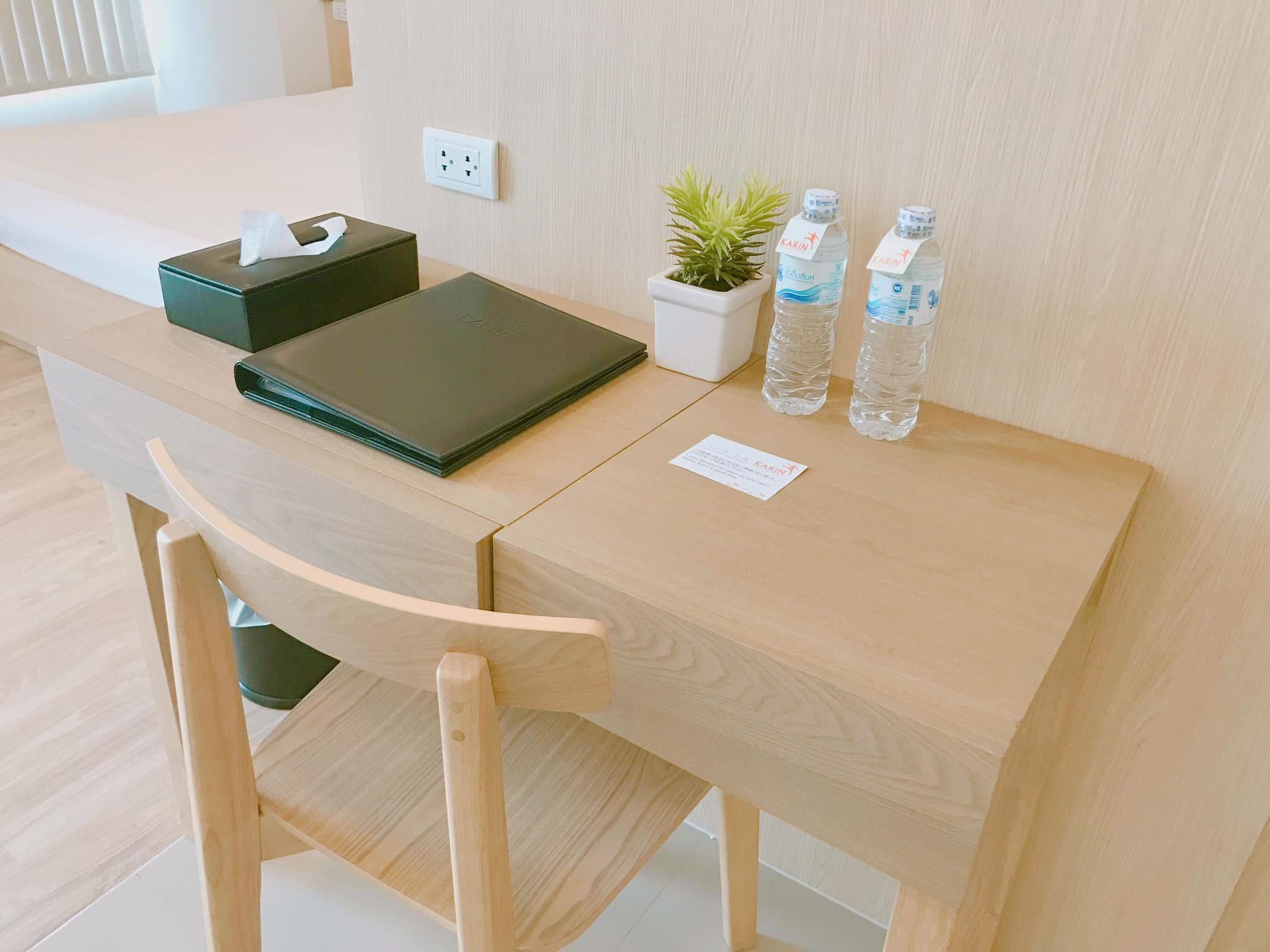 Un escritorio de madera con una caja de pañuelos, una pequeña planta en maceta y dos botellas de agua.