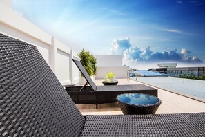 Un área de lounge en la azotea con muebles de mimbre, una piscina pequeña y una vista despejada del cielo.
