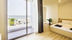 Een moderne hotelkamer met een grote glazen schuindeur naar een balkon, een netjes opgemaakt bed en een kleine plant in een pot.