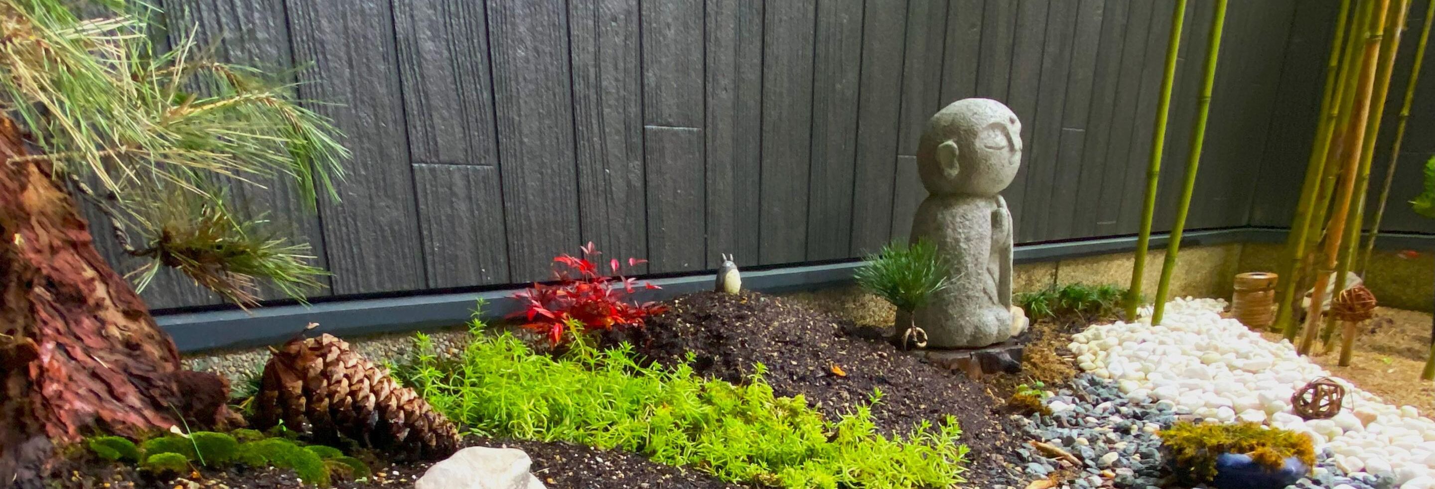 A garden with a stone statue, various plants, and a wooden fence.