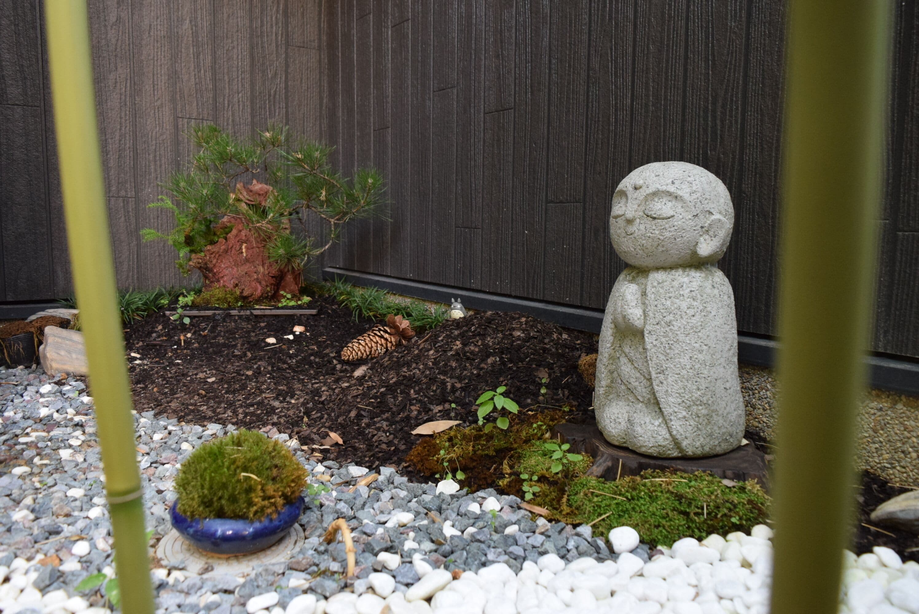 Un jardin avec une statue en pierre, un pin et un petit pot bleu.