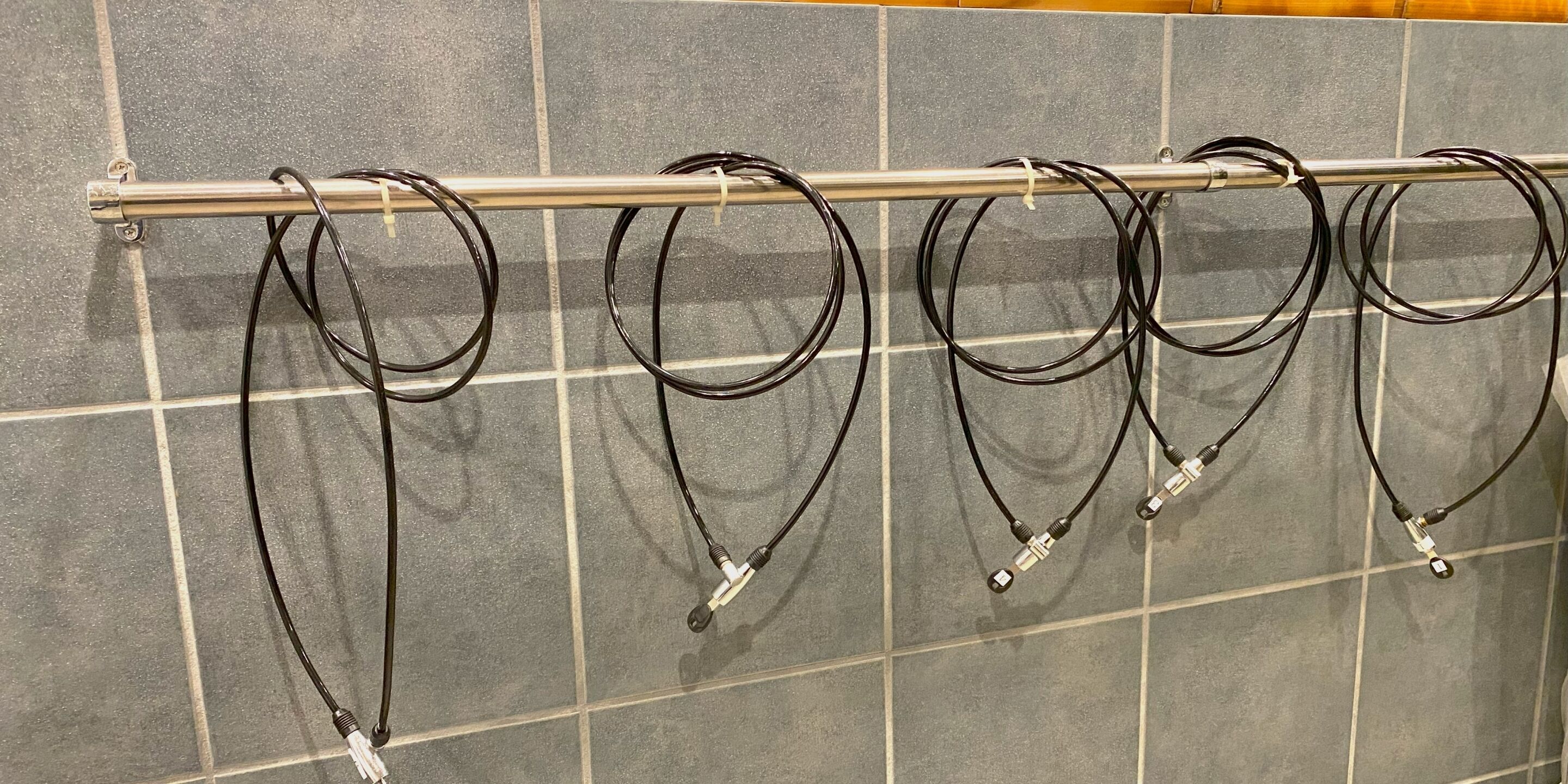 A metal rack with multiple black cables hanging from it, against a tiled wall.