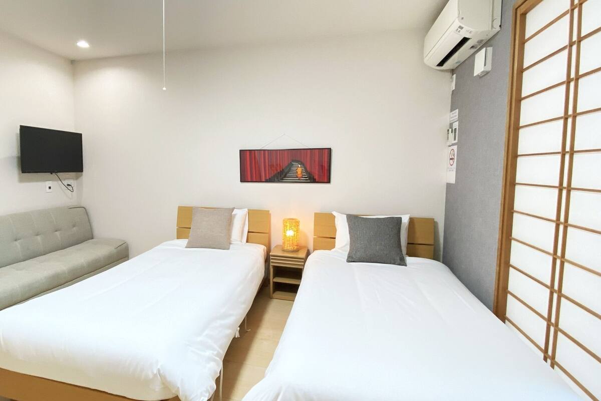 Habitación de hotel con dos camas individuales, un sofá, un televisor, un cuadro y una tradicional pantalla japonesa shoji.