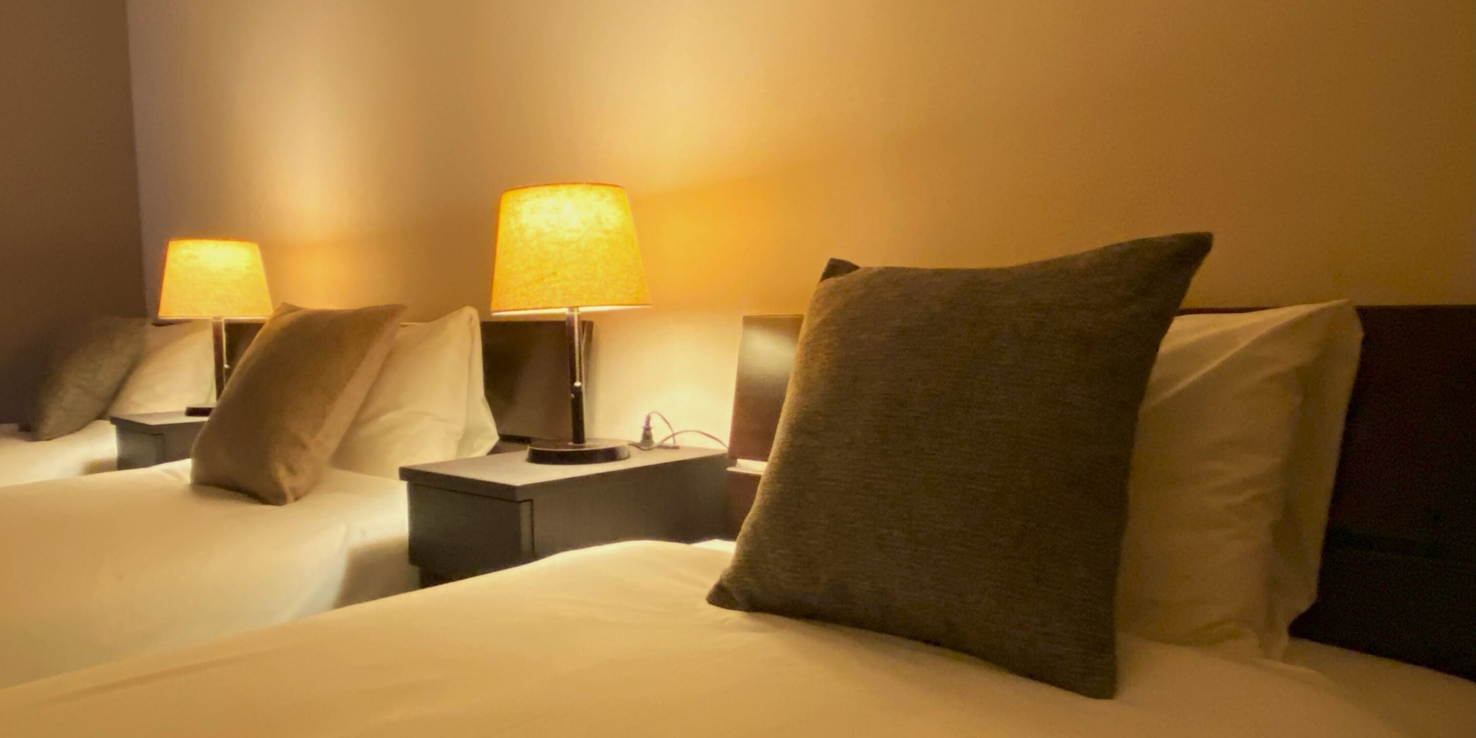 Two beds with white linens, each with a lamp and a pillow.