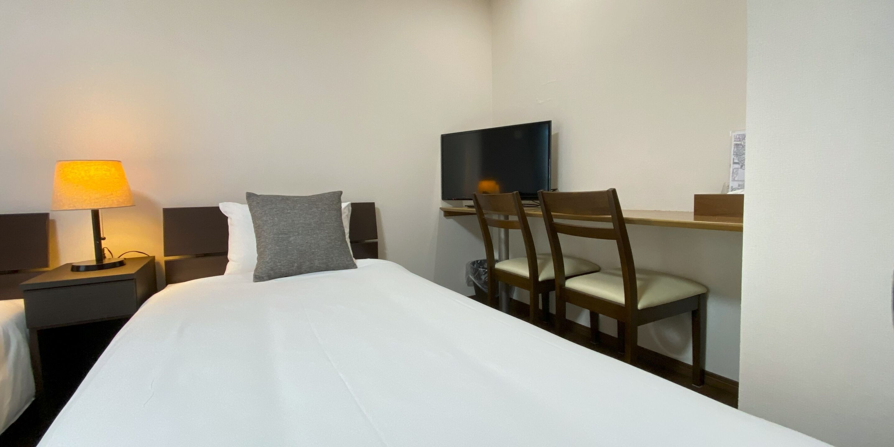 A hotel room with a bed, a desk with a chair, a television, and a lamp.