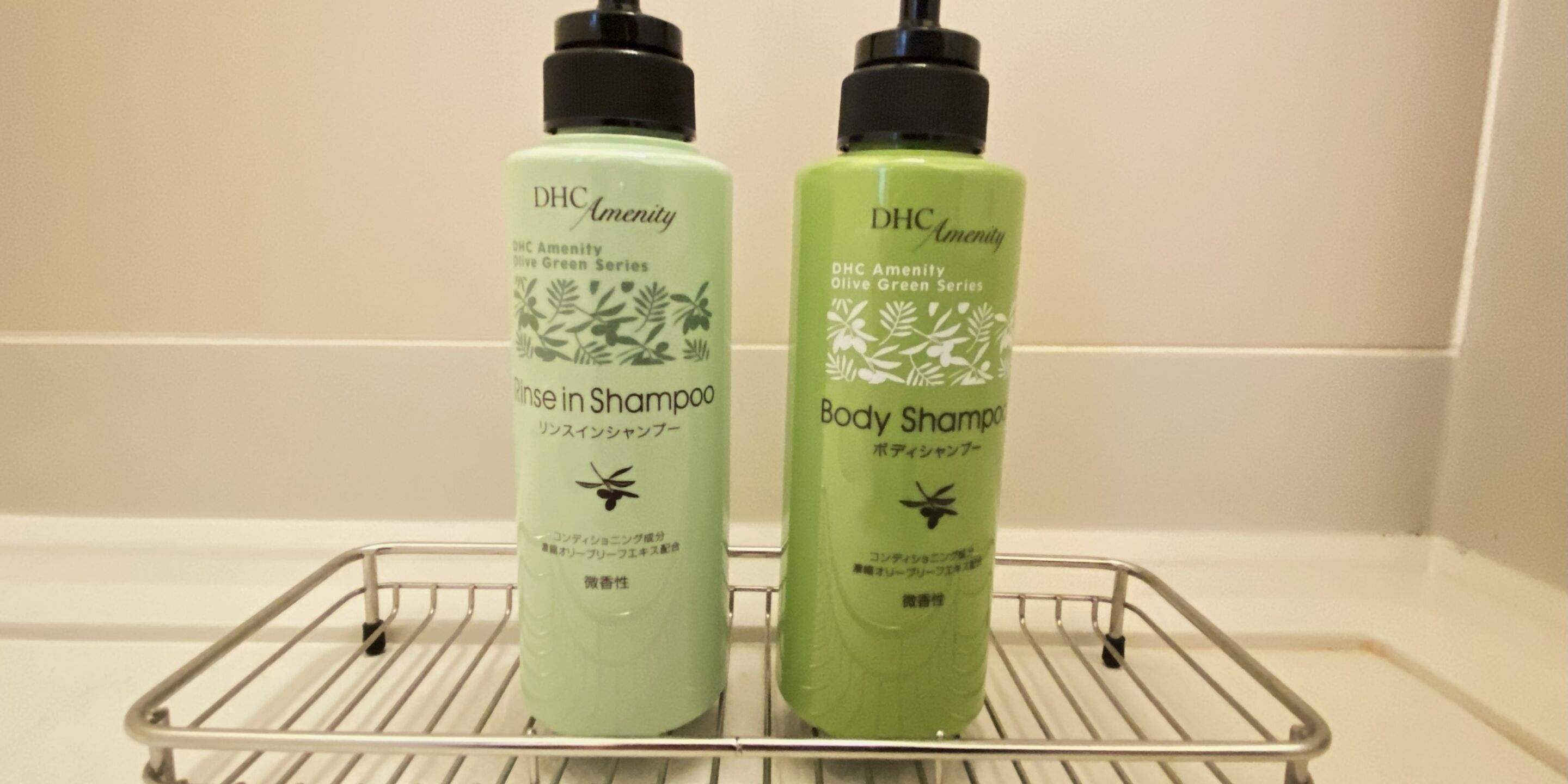 Twee flessen DHC Amenity olijfgroene serie shampoo op een metalen plank.