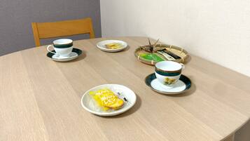 A round dining table with two white cups and saucers, a plate with a yellow item, and a basket with green and black items.