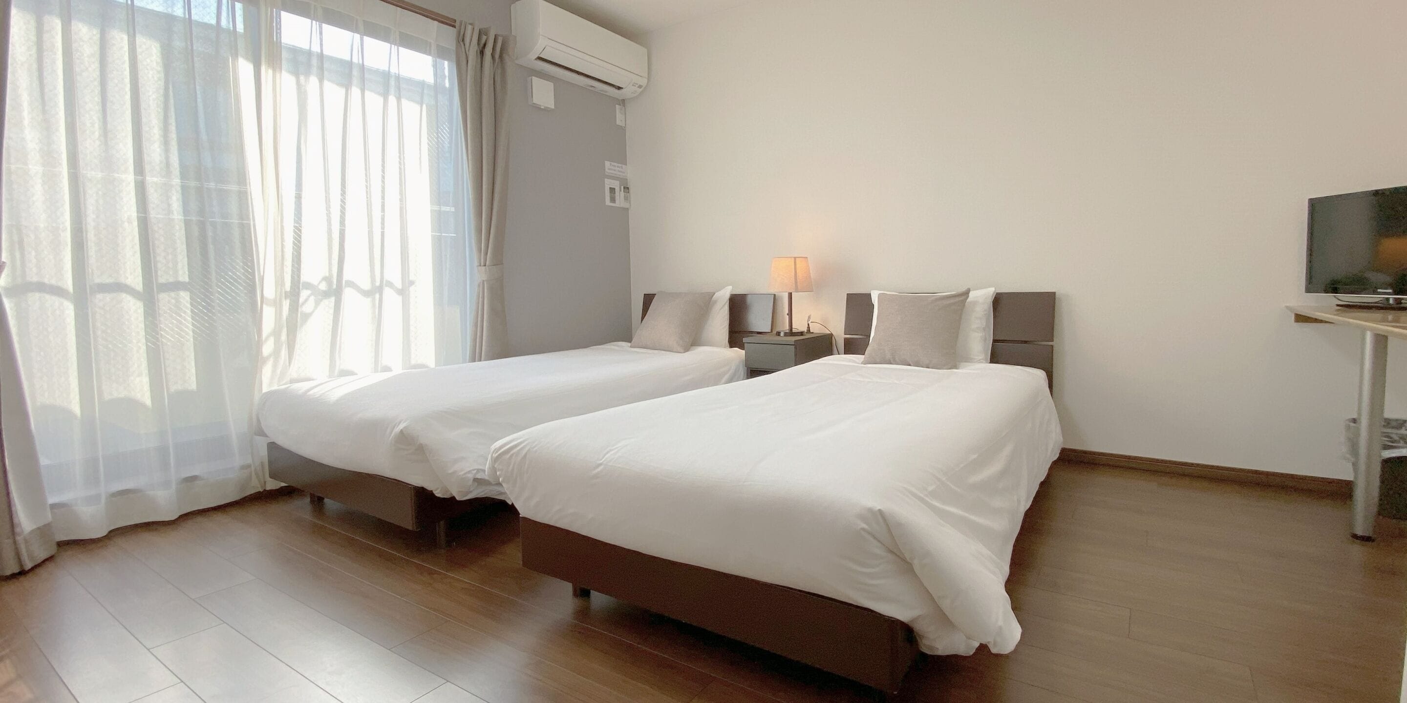 A hotel room with two beds, a TV, a lamp, and an air conditioning unit.