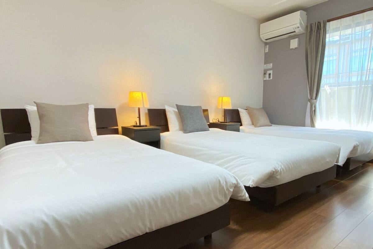 Habitación de hotel con dos camas, lámparas de noche, un equipo de aire acondicionado y un amplio ventanal con cortinas.