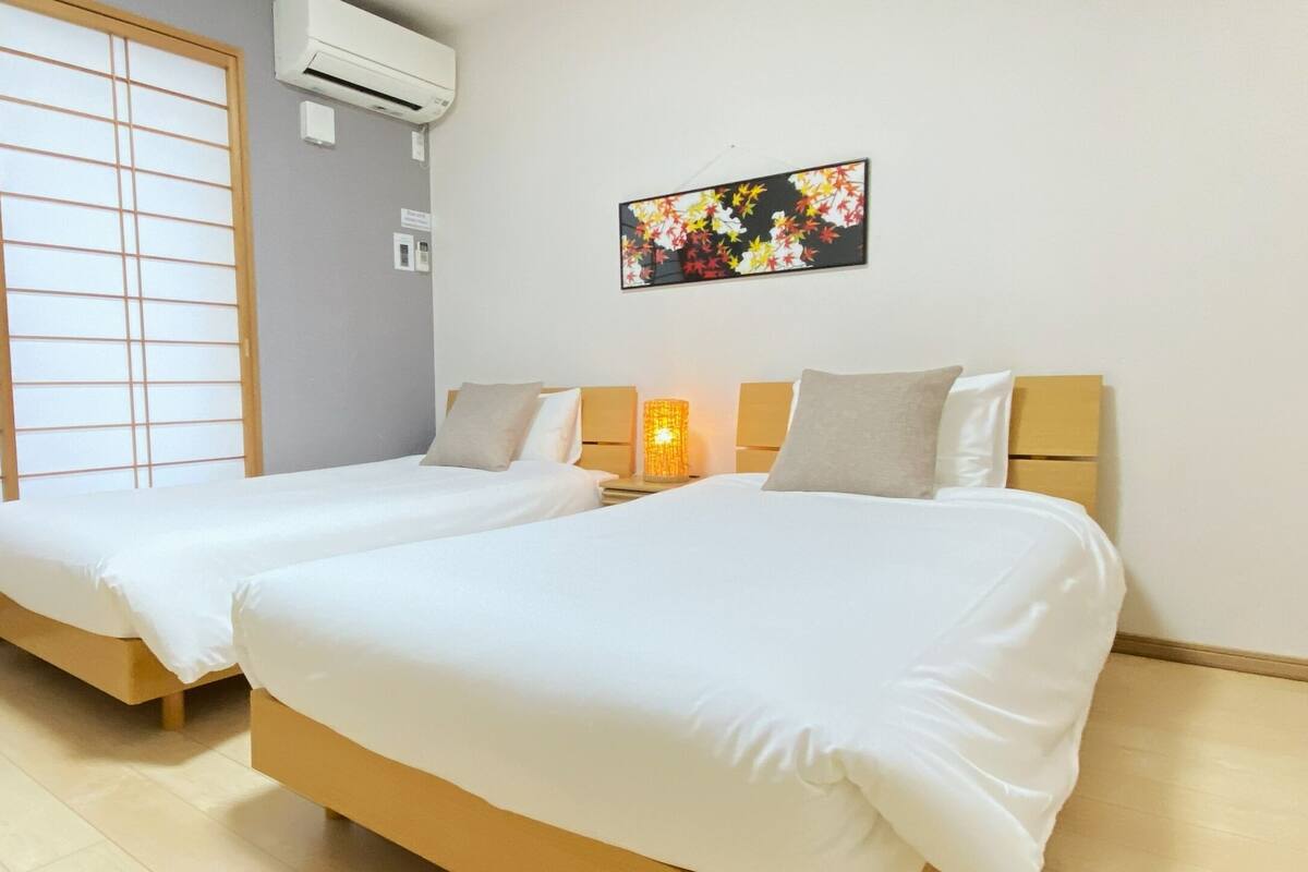 Habitación de hotel con dos camas, un separador shoji, aire acondicionado y una obra de arte colgada en la pared.