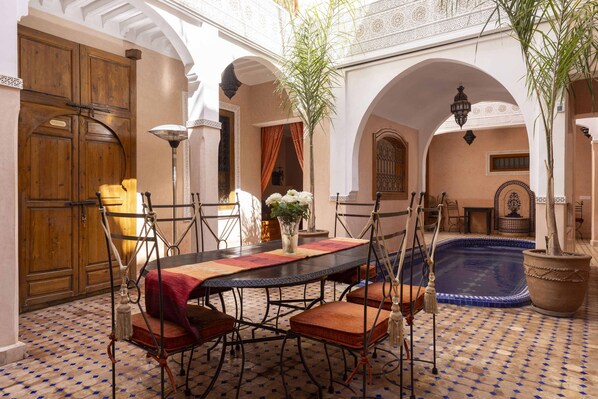 A traditional Moroccan interior with a dining area, a pool, and arches.