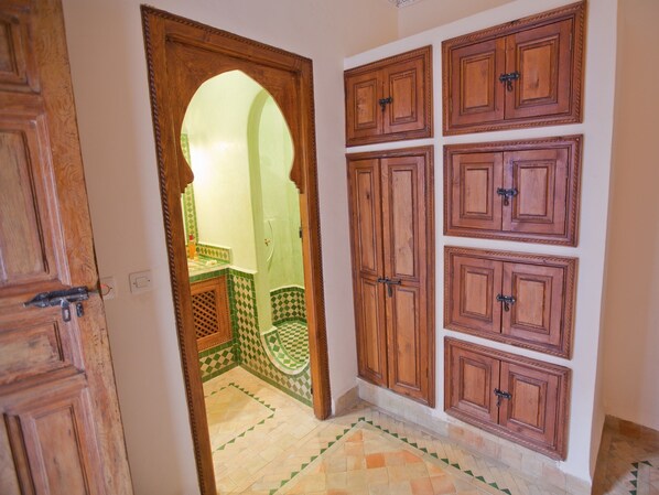 A hallway with a wooden door, a tiled floor, and a wall with multiple wooden cabinets.