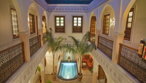 An indoor swimming pool with a central fountain, surrounded by arches and potted plants.