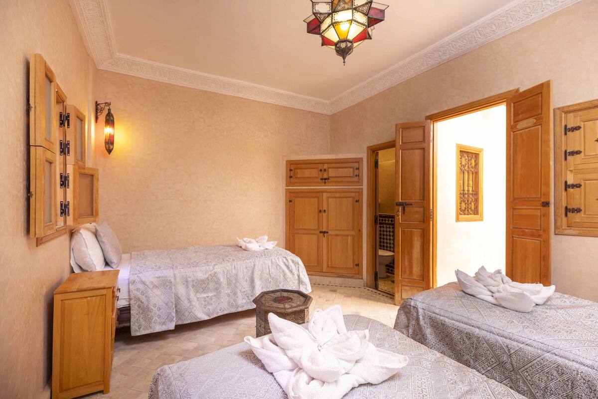 A hotel room with two beds, wooden cabinets, a small stool, and a decorative wall light.