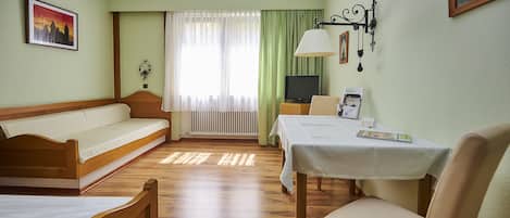 Une chambre d’hôtel avec un lit en bois, un canapé, une table à manger avec une chaise, une télévision et une fenêtre avec des rideaux.