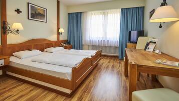A hotel room with a wooden bed, a desk, a chair, a television, and a window with curtains.