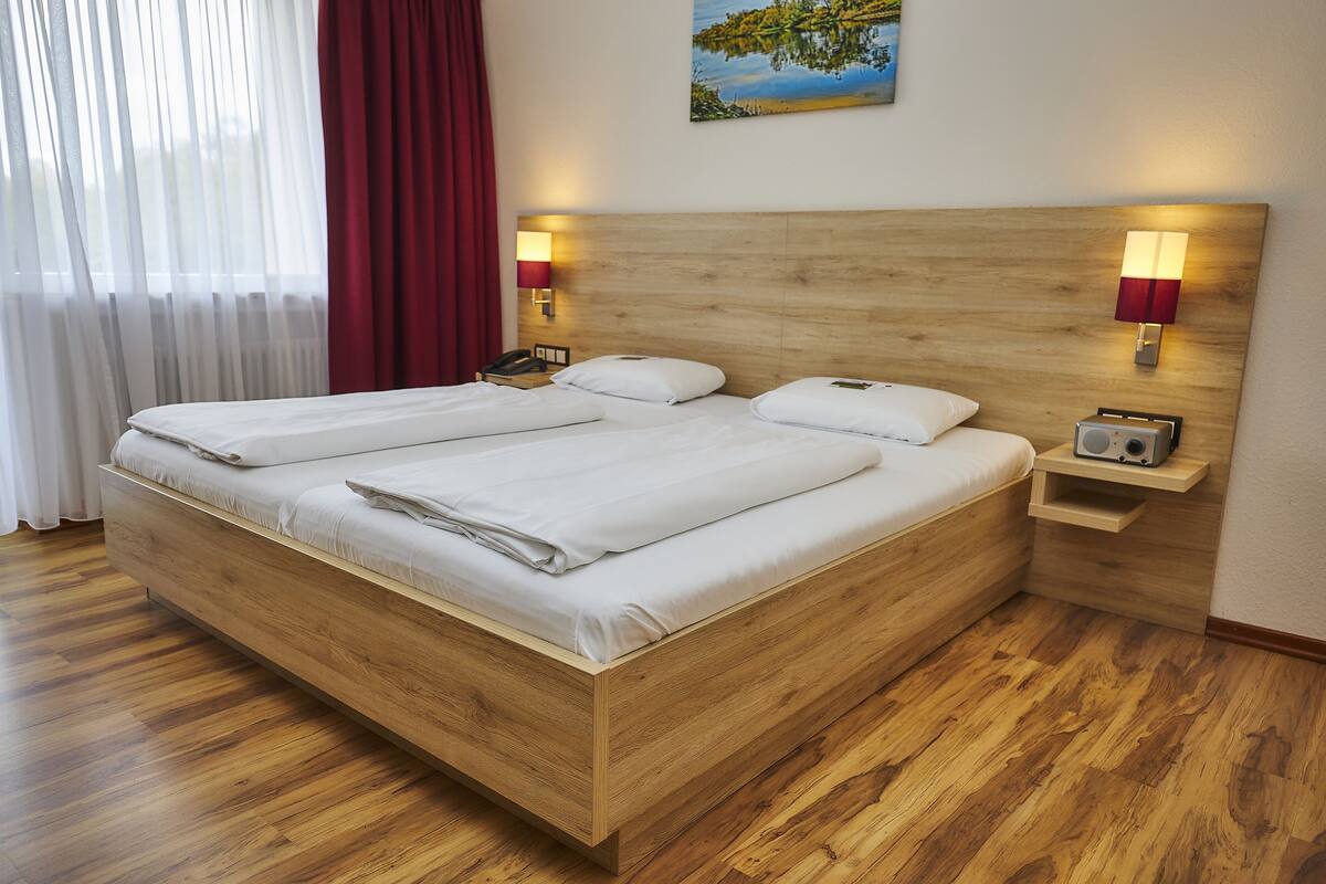 Un lit en bois avec deux oreillers, une table de chevet avec une radio et un tableau accroché au mur.