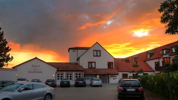 A hotel with a clear view of the sunset, a parking area with several cars, and a sign indicating the hotel name.