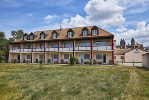 Un hotel de varios pisos con tejado de baldosas, balcones y un jardín delantero con césped.