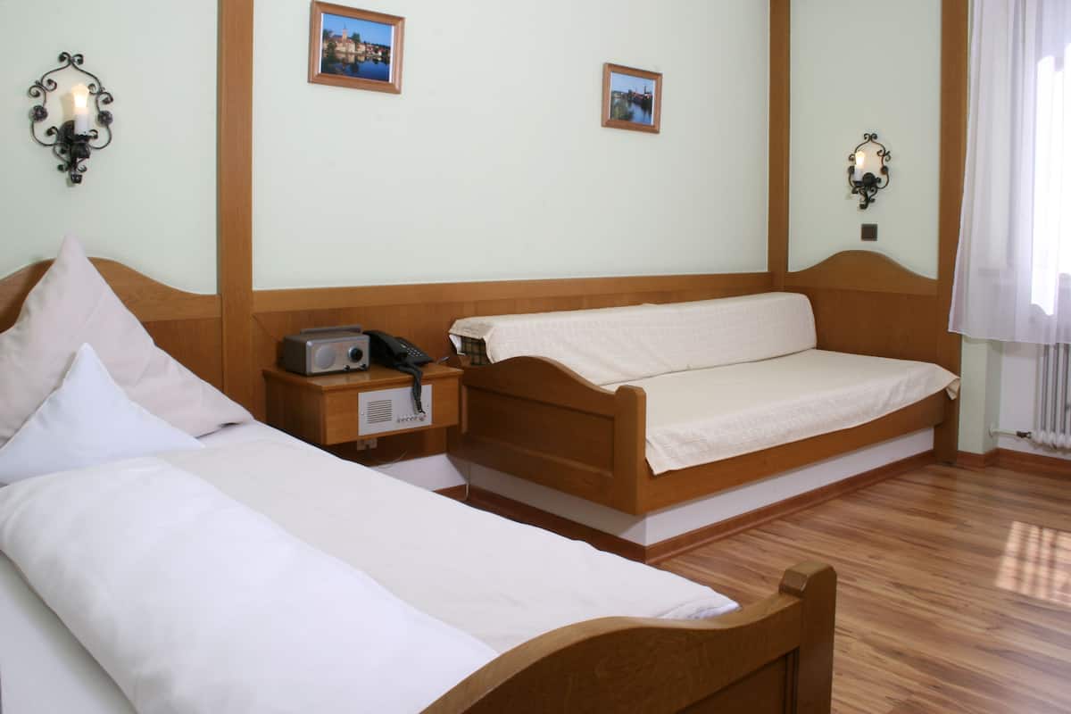 Une chambre d’hôtel avec deux lits simples, une tête de lit en bois, une table de chevet avec un téléphone et des lampes fixées au mur.