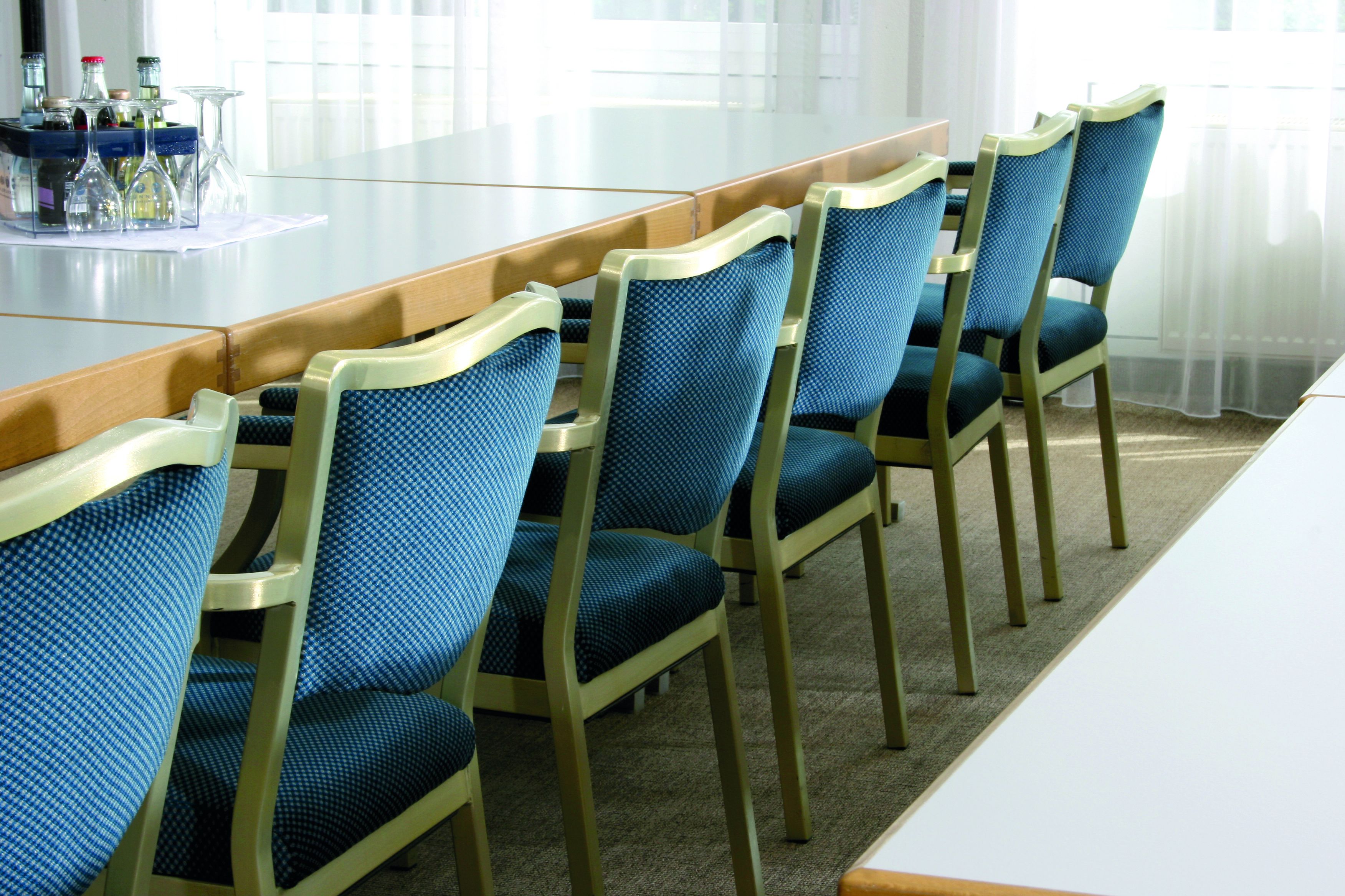 Een vergaderzaal met een lange tafel en zes blauw beklede stoelen met houten frames.