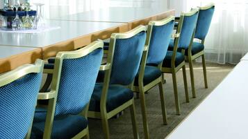 Een vergaderzaal met een lange tafel en zes blauw beklede stoelen met houten frames.