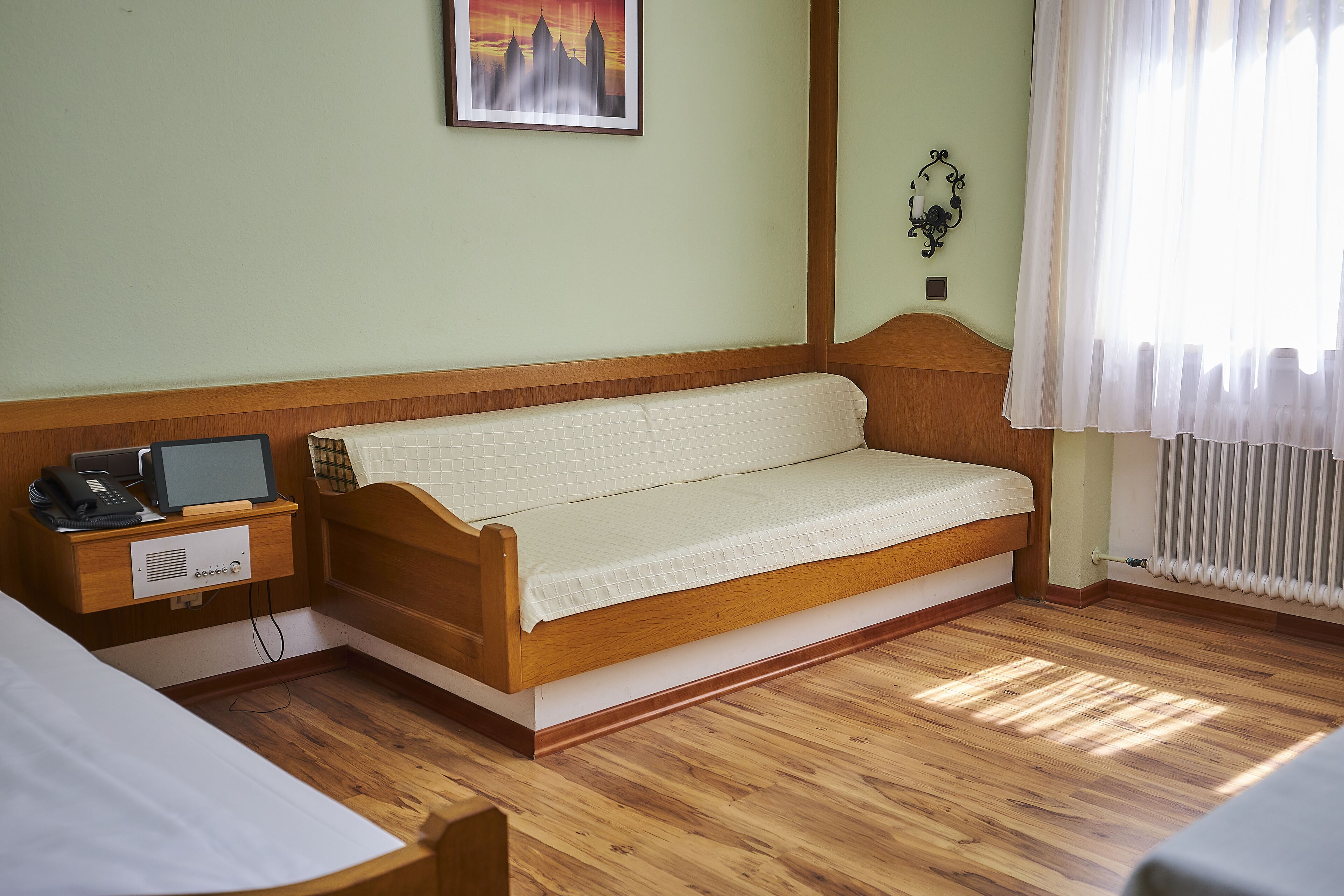 Una habitación con una cama de madera, una mesita de noche con una lámpara, un cuadro en la pared y una ventana con cortinas.