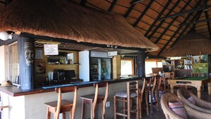 A bar area with wooden stools, a pool table, and a thatched roof. - Roaring Sky (Cullinan)