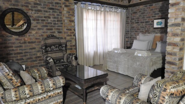 A room with a brick wall, a bed with white bedding, a patterned sofa, and a small table. - Roaring Sky (Cullinan)